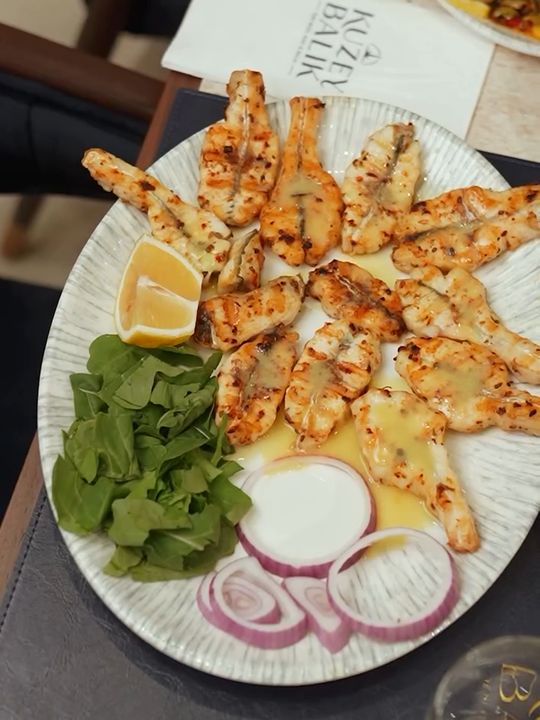Roka, limon ve kırmızı soğanla servis edilen ızgara balık filetoları